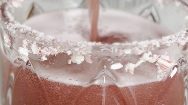 A red holiday margarita in a glass with candy canes rimming the glass
