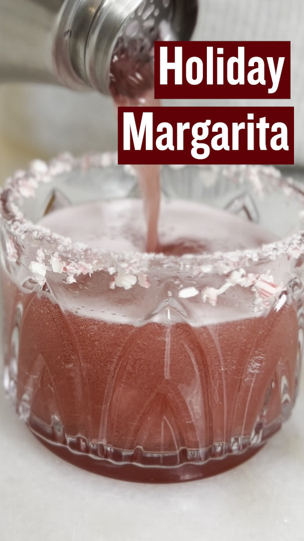 A red holiday margarita in a glass with candy canes rimming the glass