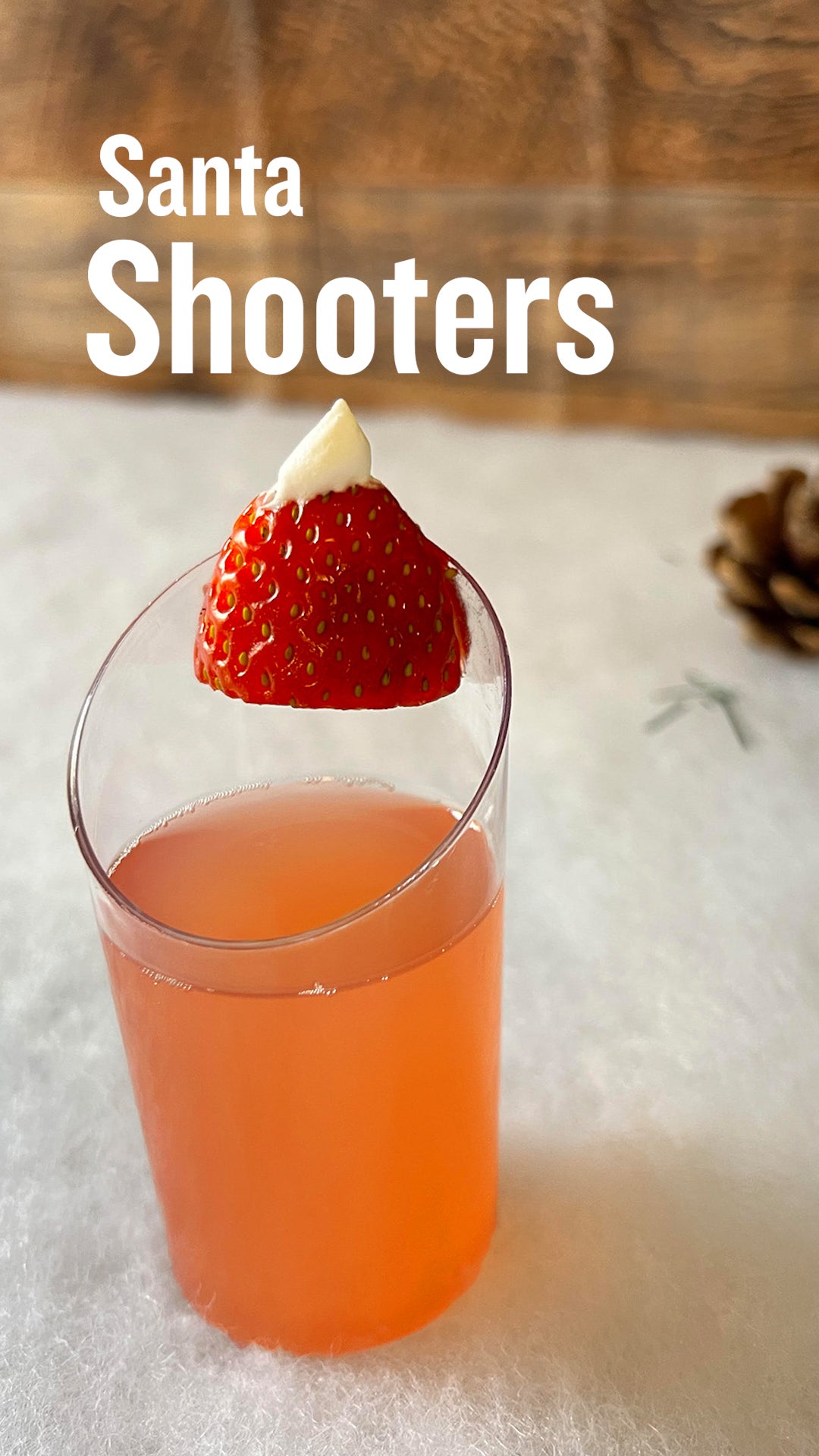 a cocktail shooter filled with red strawberry margarita mix and tequila. It has a cocktail garnish of a strawberry and dollop of Cool Whip to resemble the hat of Santa Claus